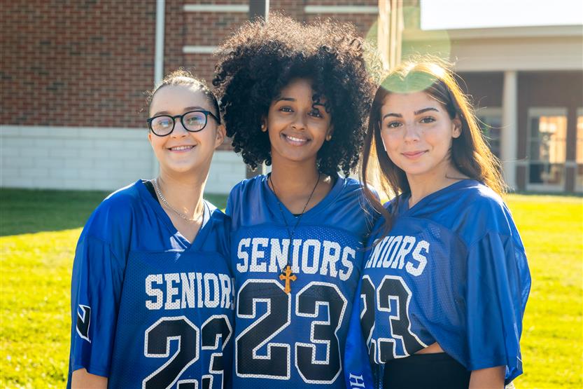 Three students wearing blue smile